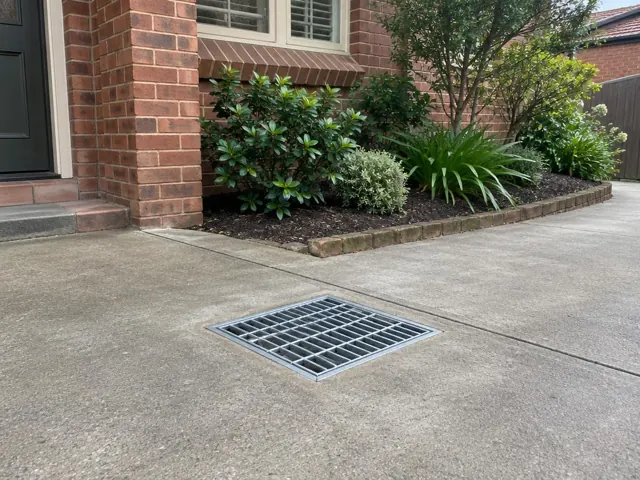 Outdoor driveway drain grate beside brick house and garden bed in Chatswood