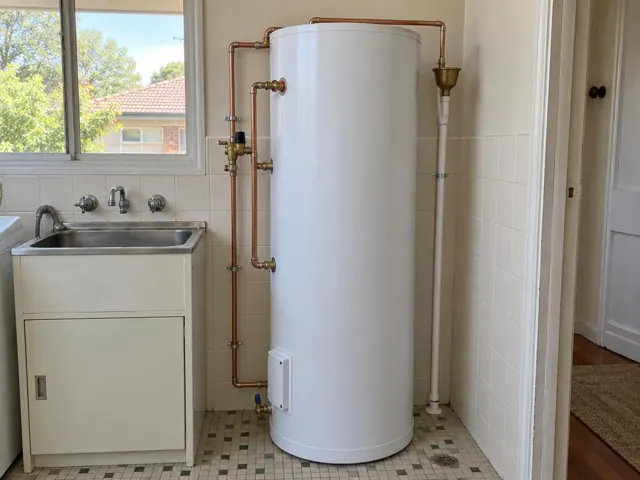 White hot water tank with copper pipework in a tiled laundry beside a sink in Willoughby